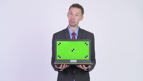 Studio Shot of Happy Businessman Showing Laptop and Looking Surprised