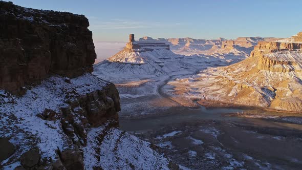 Aerial view flying along cliff revealing snowy desert landscape with river