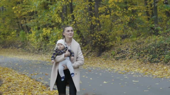 Happy Mother Holds Her Little Baby Son in Embraces Smiling and Walking at Park