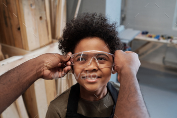 ving protective goggles to cute son helping father in workshop