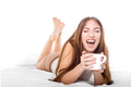 Attractive woman with a cup of coffee on the bed. Laughing from ear to ear - PhotoDune Item for Sale