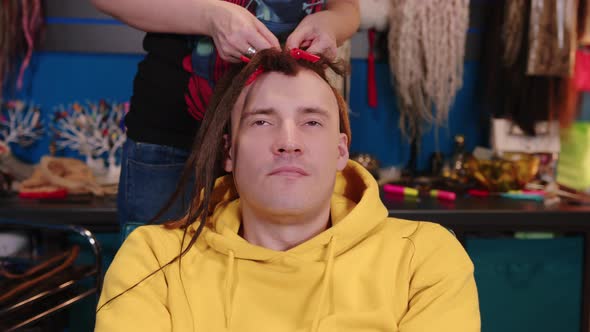 Unrecognizable person makes hairstyle for young man in salon.
