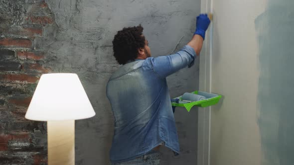 Young Black Painter in Denim Clothes Paints Room Corner