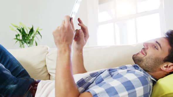 Man using digital tablet while relaxing on sofa