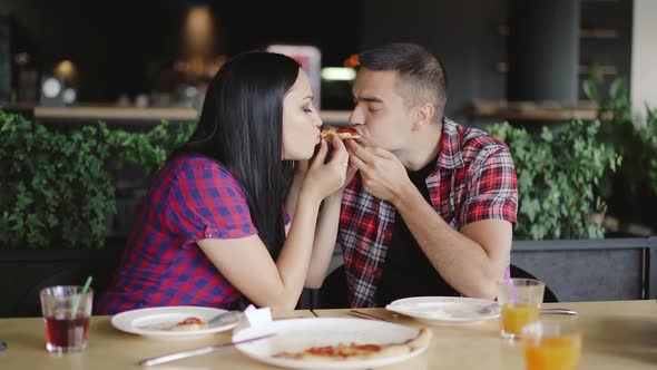 romantic couple are eating one slice of pizza together in the pizzeria