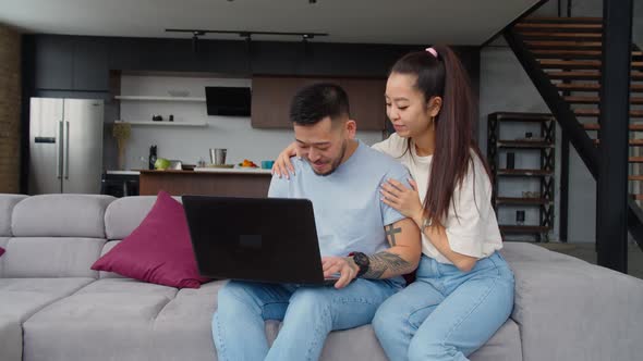 Loving Asian Couple Browsing Online on Laptop at Home