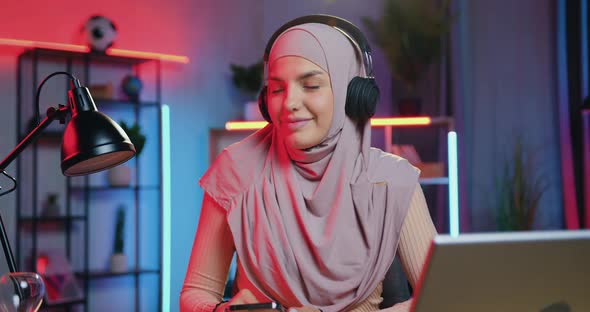 Lady in Hijab in Headphones Listening Music in Beautifully Decorated Room with Colourful lighting