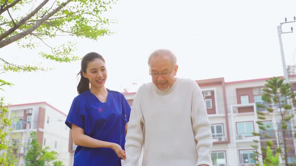 Asian young caregiver nurse support senior older male walking outdoors.