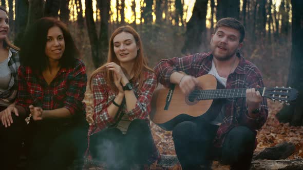 Happy Tourists Playing Guitar By Campfire in Autumn Forest