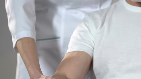 Nurse Helping Old Man With Trembling Hands Holding Dumbbells, Rehabilitation