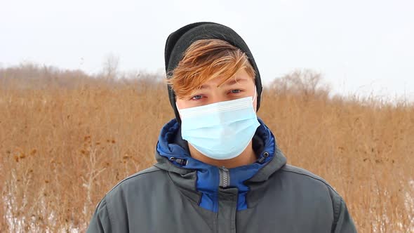 a Young Caucasian Teenager Man Dressed in Warm Winter Clothes Stands on the Street in a Blue Medical