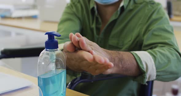 Man wearing face mask sanitizing his hands at office