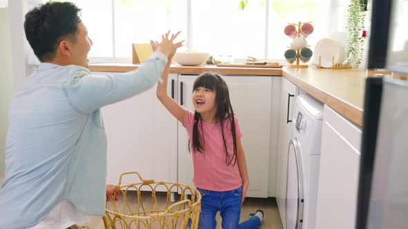 Asian young little cute girl child help and learn from parent dad to put laundry in washer appliance