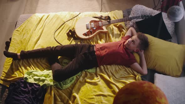 Teen Guitarist Relaxing on Bed