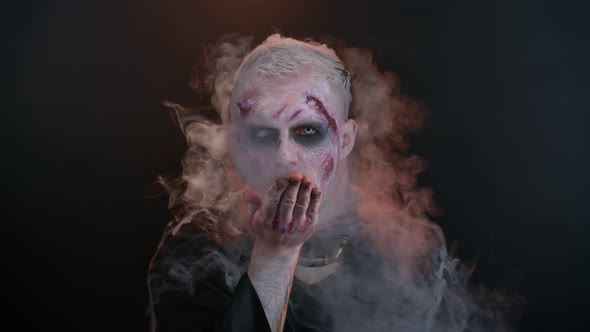 Sinister Man Halloween Zombie with Bloody Face Blows Smoke From Nose and Mouth Making Air Fly Kiss