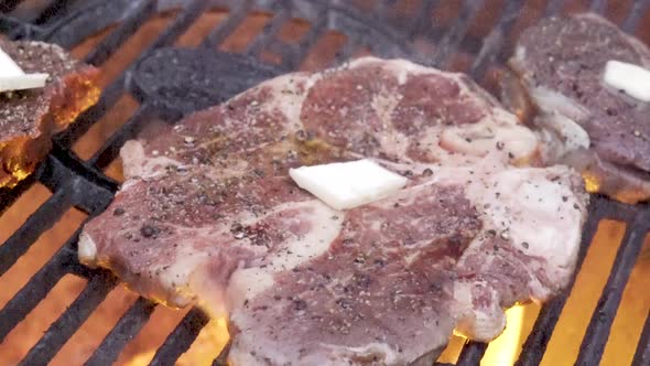 Large slab of raw t-bone steak with pads of butter and sprinkle of pepper on it on the grill with fl