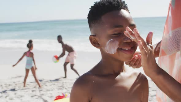 Smiling african american family using sun cream on sunny beach
