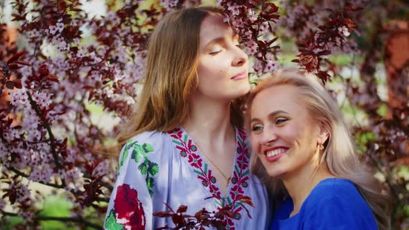 Two Happy Woman Have Fun on the Background of Blooming Pink Sakura Flowers