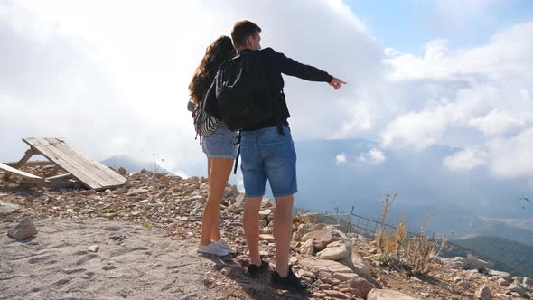 Couple of Hikers with Backpacks Standing on Mountain Edge and Enjoying Landscape