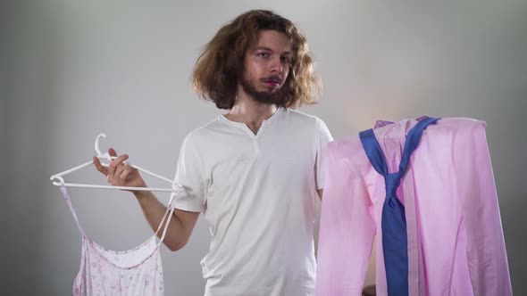Portrait of Young Caucasian Intersex Person Choosing Outfit Between Women's Dress and Male Shirt