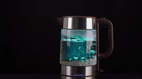 A Modern Glass Electric Kettle on a Black Background Filled with Water to Boil
