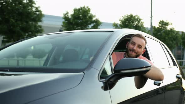 A Young Man with Beard Looks Out of the Car Window Smiles and Gives Thumbs Up