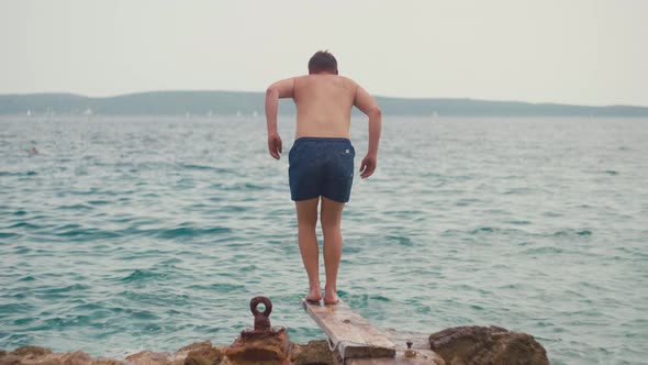 Lifestyle Slow Motion Video of a Guy Jumping From a Pier Into the Sea Water