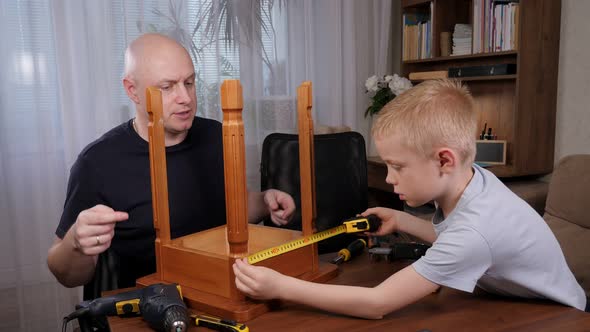 A Boy with His Father is Repairing a Chair the Boy is Using a Measuring Tape