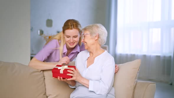 Young daughter giving a present to a elderly mother at home