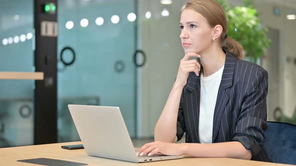 Attractive Young Businesswoman Thinking and Working on Laptop in Office