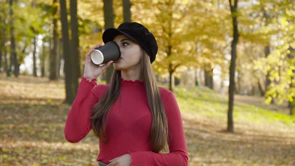 Happy Girl in Stylish Look Posing and Drinking a Cup of Tea in Sunny Autumn Park