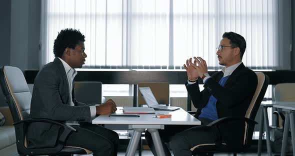 Two Young Businessman Talking at Desk in Office