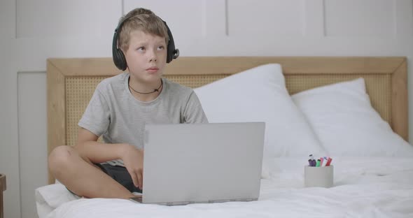 Little Boy Is Chatting with Parents Online By Laptop with Headphones From Summer Camp, Sitting on