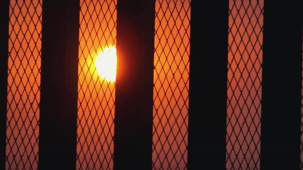 Wide Time Lapse Shot of The Sun Setting in and Orange Sky Through Very Close Fence