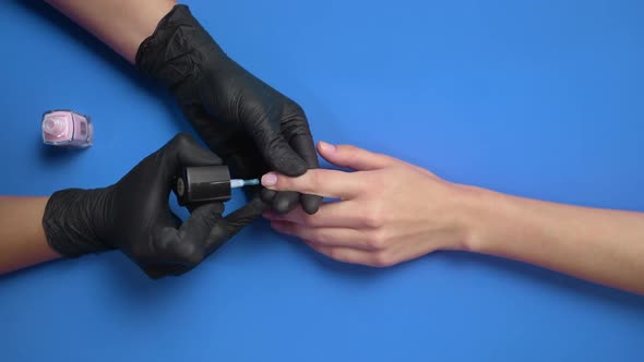 Manicurist in Black Rubber Gloves Paints Client's Nails with Transparent Protective Nail Polish