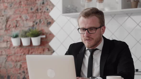 Young American Businessman Is Having Conversation and Working with Laptop at Table in Home.