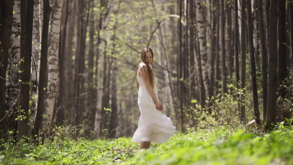 Young Romantic Woman in a White Light Dress Posing in the Forest Among Birches