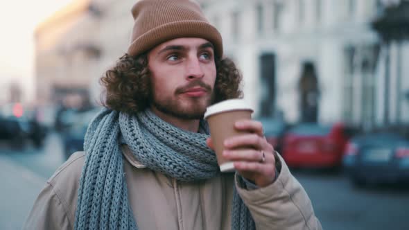 Positive curly-haired man drinking coffee and looking around
