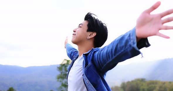 Freedom Asian young man raising hands on the top at the mountain.