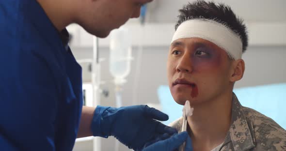 Close Up of Doctor Cleaning Wound on Face of Asian Soldier in Army Hospital