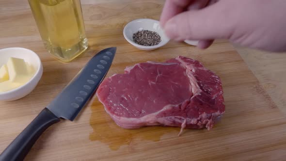 Slow Motion Slider Shot of Seasoning a Ribeye Steak With Salt on a Wooden Cutting Board Prior to Coo