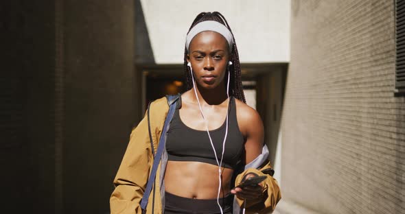 Portrait of african american woman exercising outdoors wearing earphones and smiling to camera