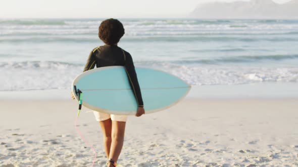 African american woman walking with surfboard on sunny beach