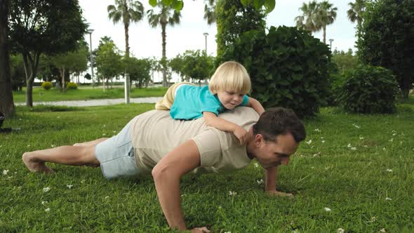 Child Climbs on the Father's Back While Father Does Pushups From the Floor in the Park