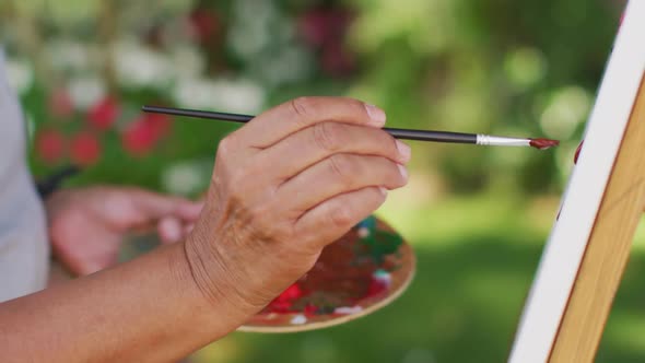 Video of hands of biracial senior woman painting in garden