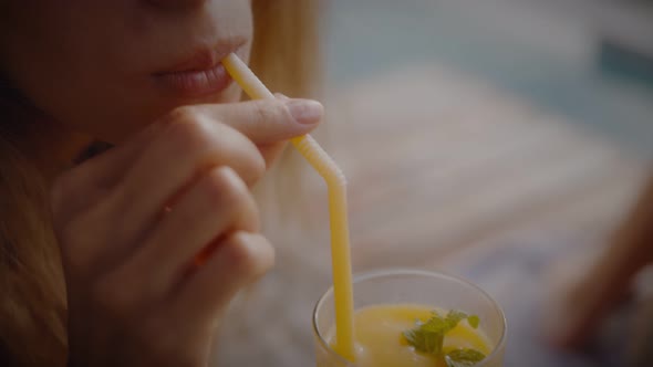 A Blonde Woman Drinks Mango Shake While Lounging in the Sun By the Pool on Vacation