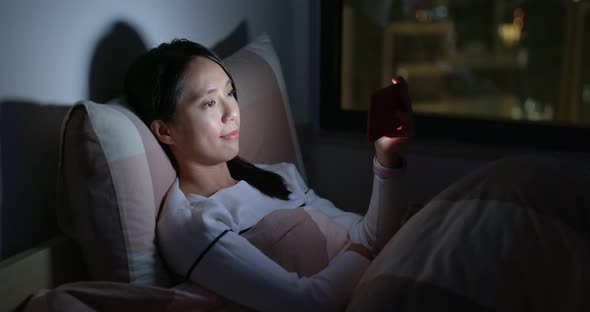 Woman watch on cellphone on bed at night