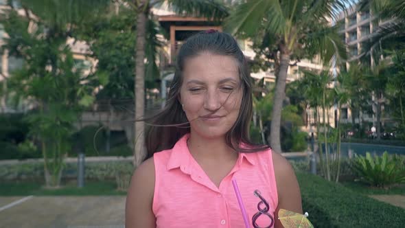 Nice Girl in Pink Blouse Stands Against Palms Smiling