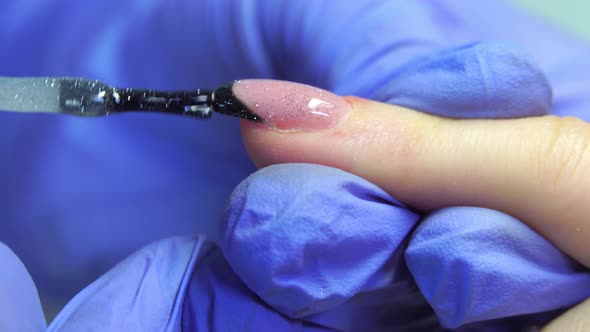 Close-up of manicure master applies shiny layer with sequins to client's nail.