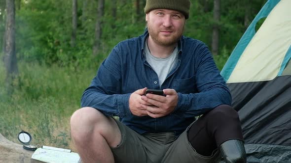 male tourist with prosthetic limb sits on log uses phone to write message